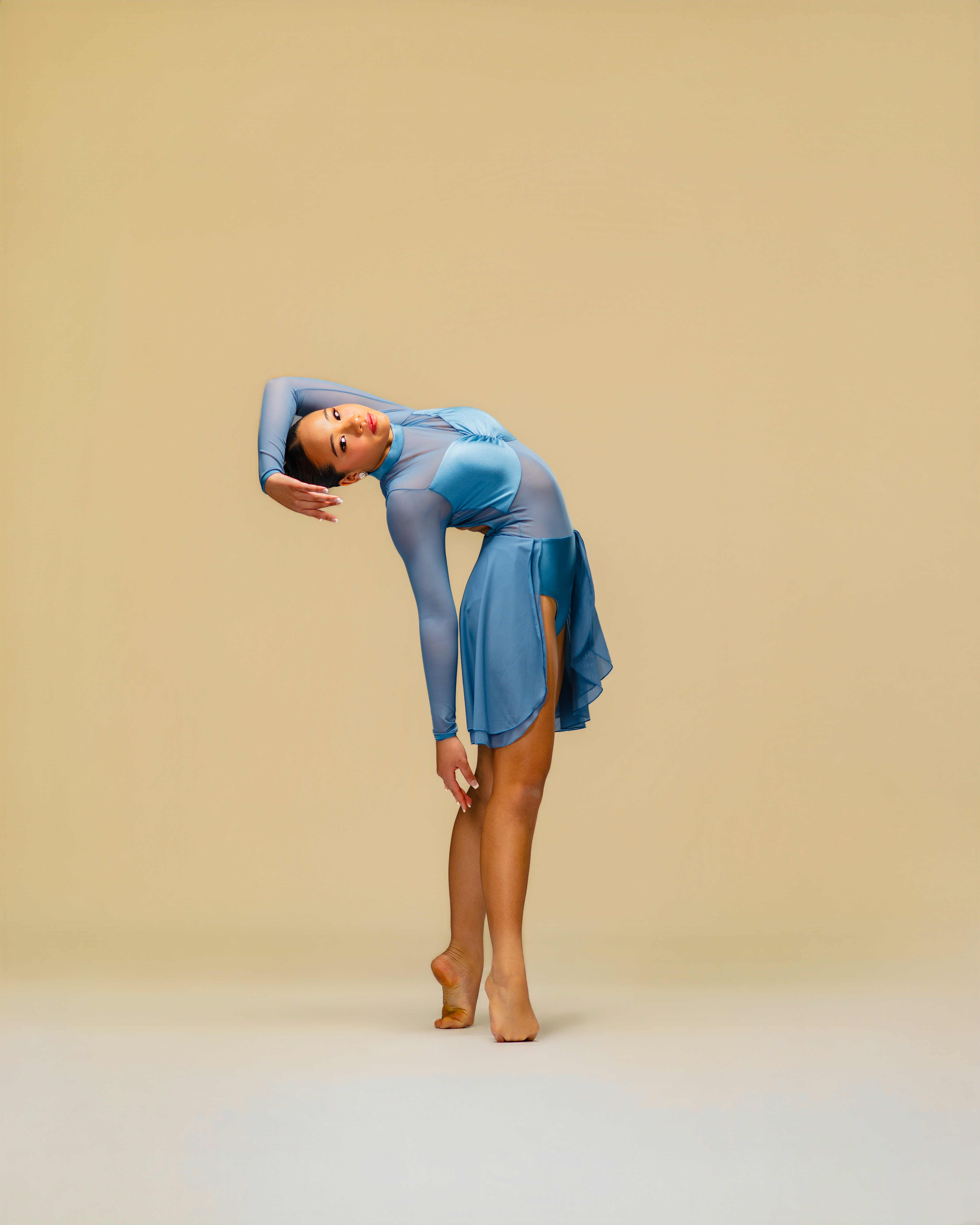 Richani Luong in a dusty blue mesh lyrical dress, arching sideways with one arm framing her head