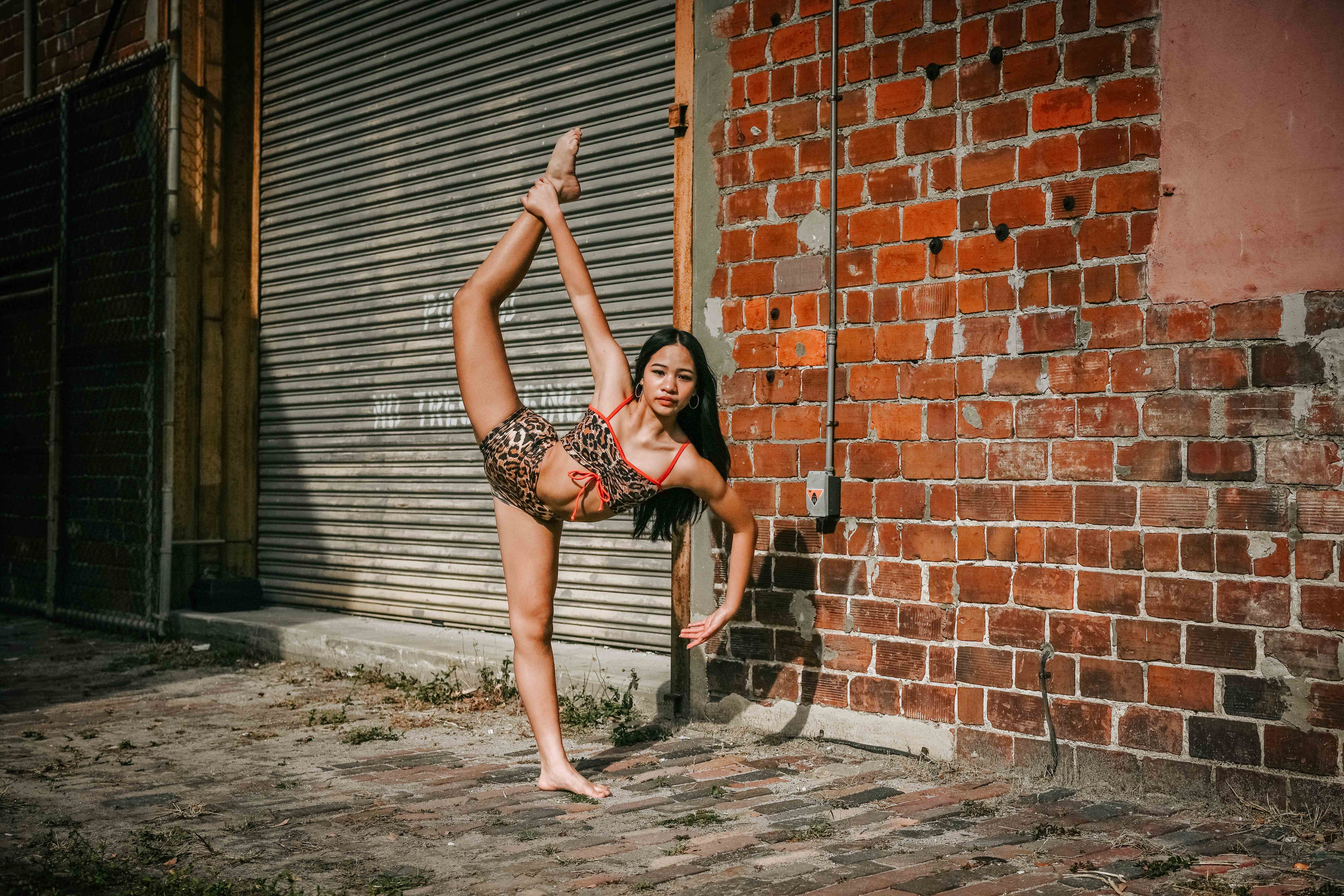 Richani in a standing leg hold beside a red brick wall