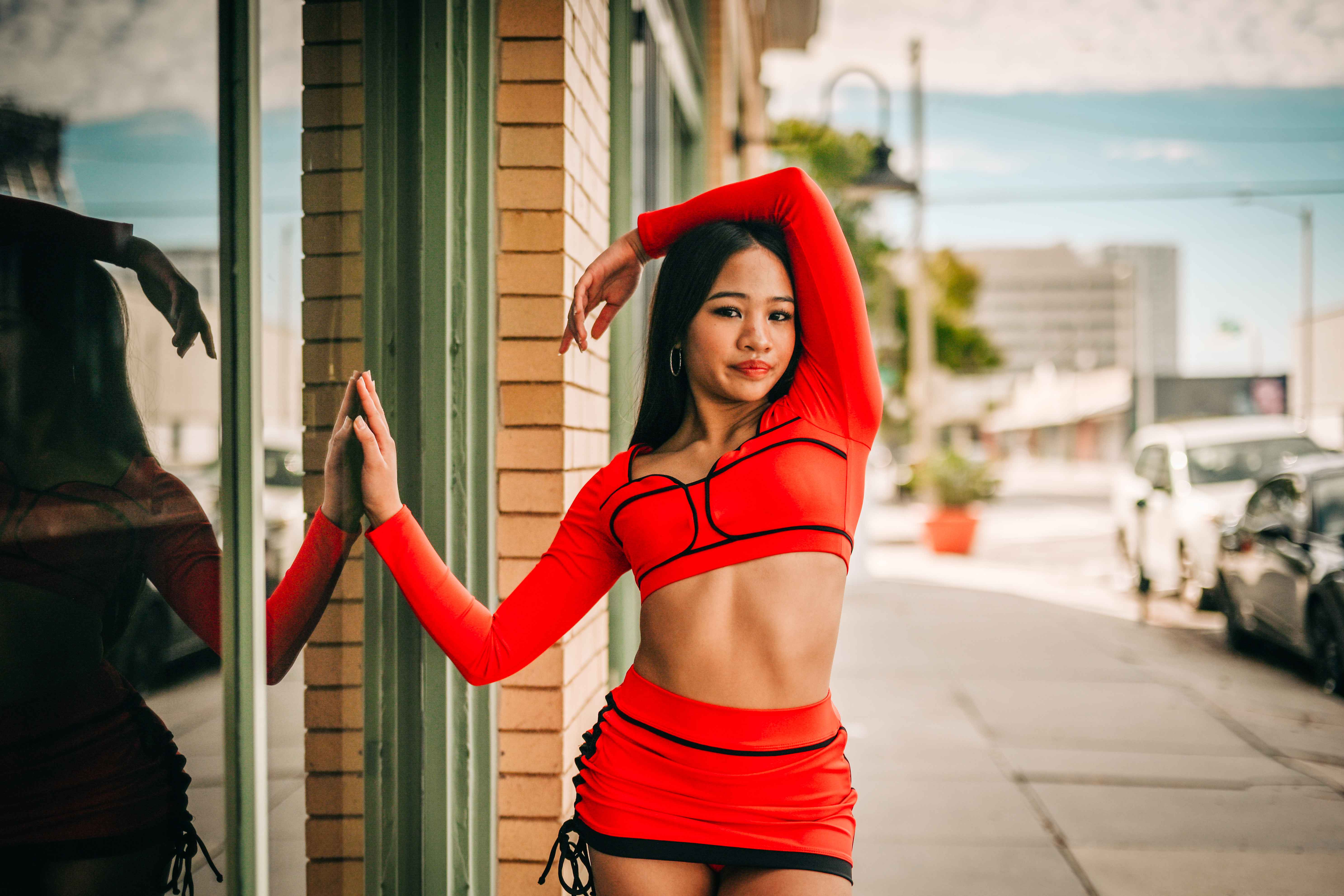 Richani posing with an arm over her head beside a reflective storefront window