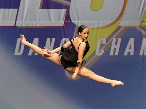 Richani mid-air in a split leap on a competition stage